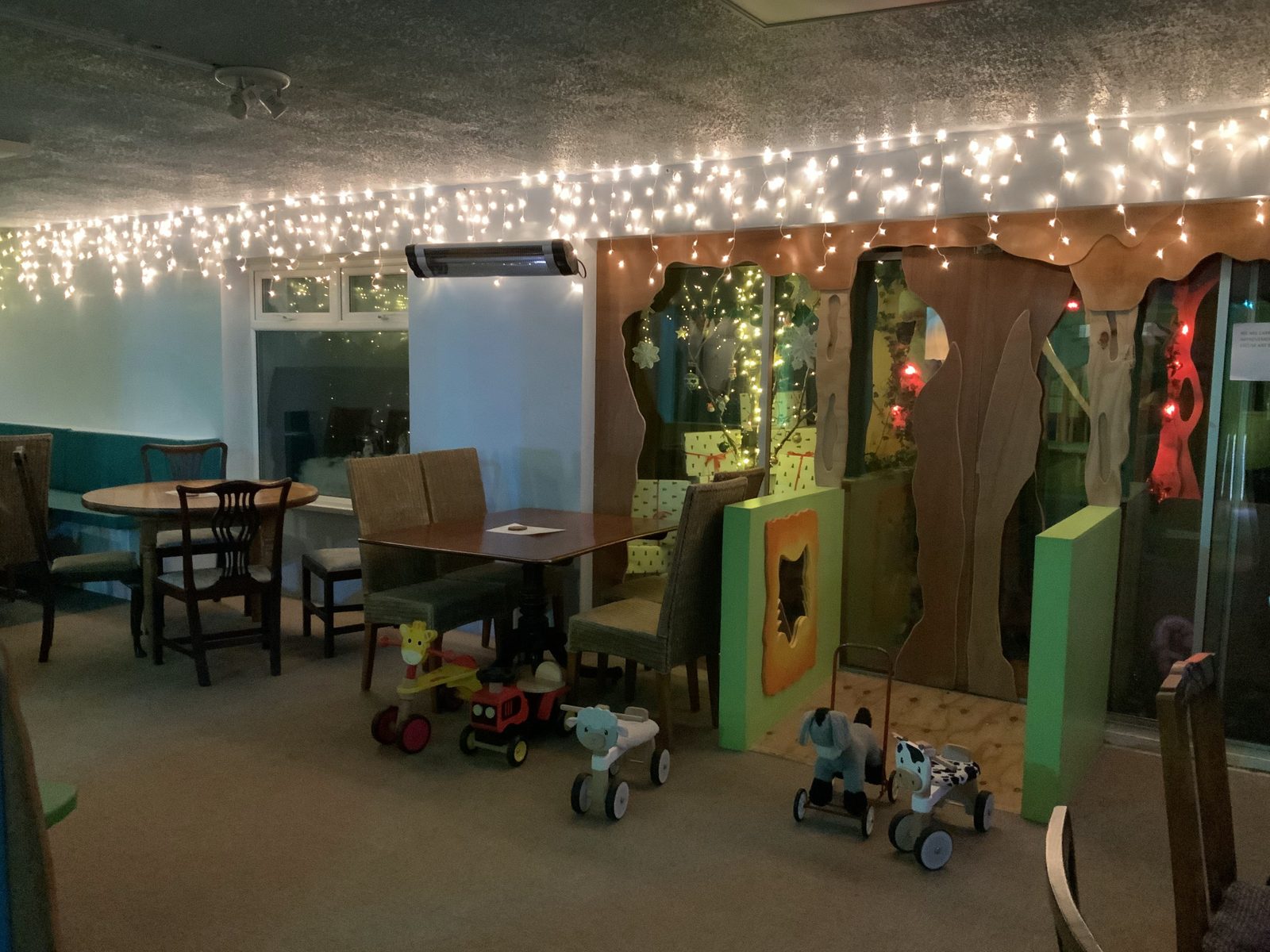 The indoor play room lit with fairy lights, with ride-on toys and seating for grown-ups